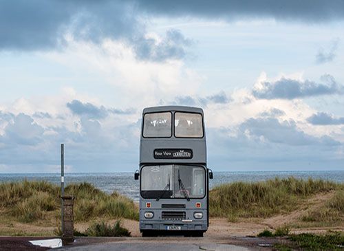 Image of front of bus on seafront. Sign on the front says 'Rear View Out There'