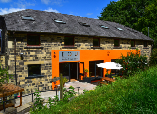 There is a large stone building, with a bright orange panel on the front. There are trees in the background, and a blue sky above the trees.