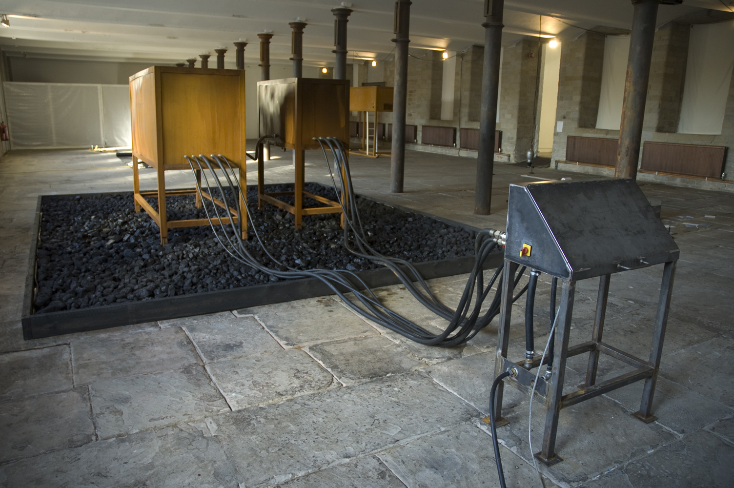 Two wooden desk like structures sit in the middle of a large room. There are dark grey wires coming out of them.