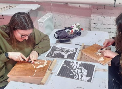 A woman sits at a table making a wood carving from a black and white illustration