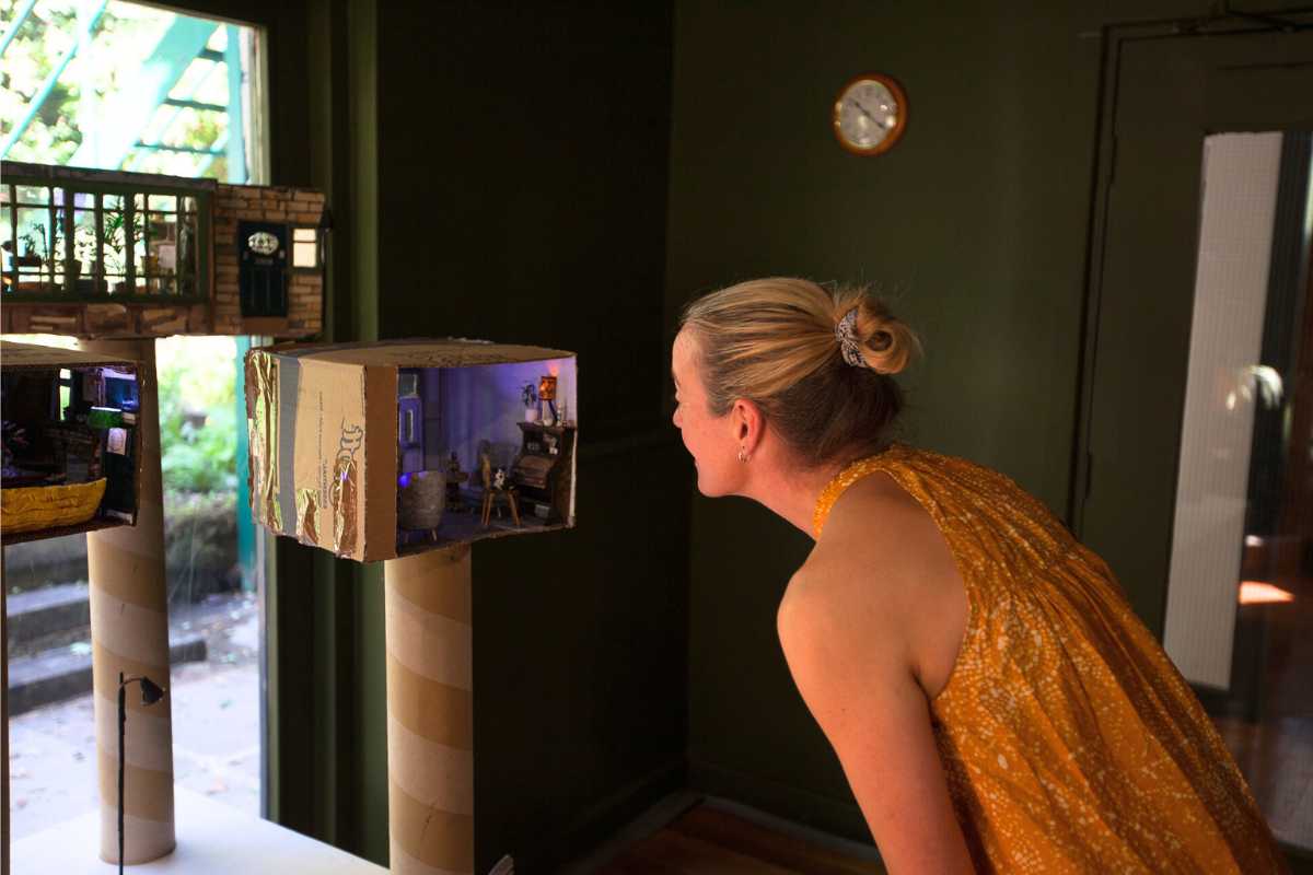 woman looks into a box containing a tiny model of a living room